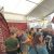 Crowded exhibition booth under a white tent with red banners; attendees browse products and chat with staff.