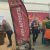 Tall curved red ASN Autositze banner at an indoor car show booth, with a Jeep graphic at the bottom and sawdust on the floor.