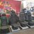 Row of automotive seats on metal pedestals at a trade show booth, with a red backdrop featuring graphics in the background.