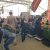 People at a trade show examining car seats displayed on platforms inside a large tent with banners overhead.