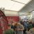 Crowd of attendees at an automotive expo inside a large tent, red banners and metal truss structures nearby.